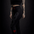 Woman in black outfit with tattoos and red heart designs on a dark background