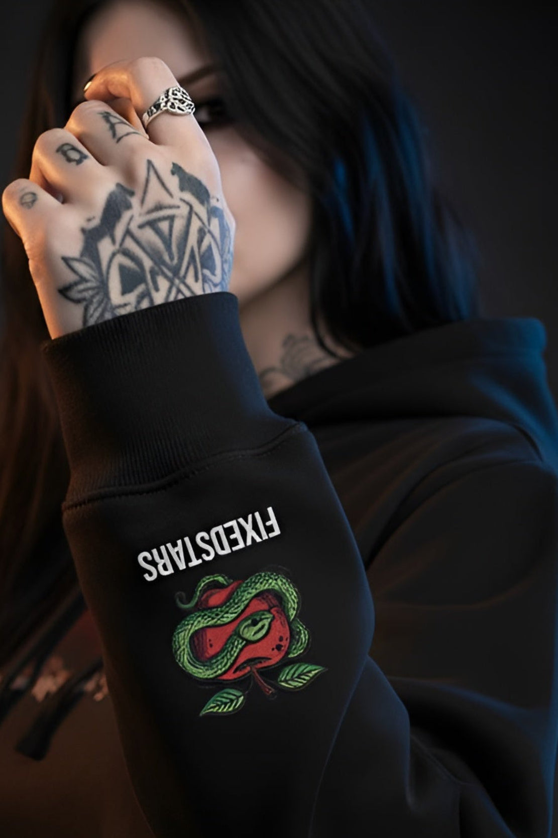 Person wearing a black hoodie with a snake emblem and text, holding hand up to face.